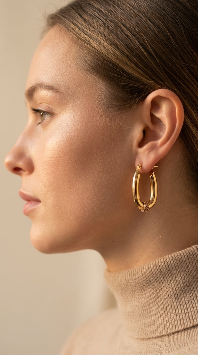 Close-up of a person wearing gold hoop earrings with a neutral background