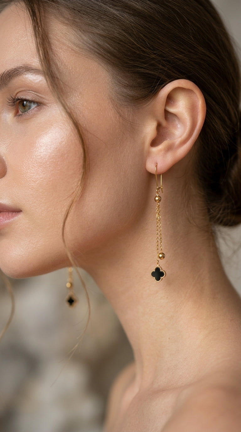 Close-up of a woman wearing gold earrings with black clover pendants.