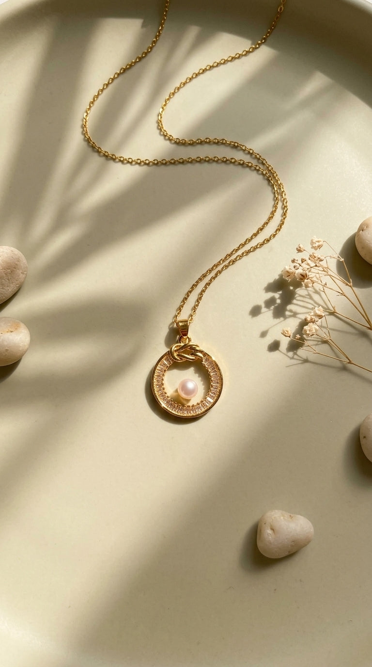 Gold necklace with a pendant on a light surface with stones and dried plants