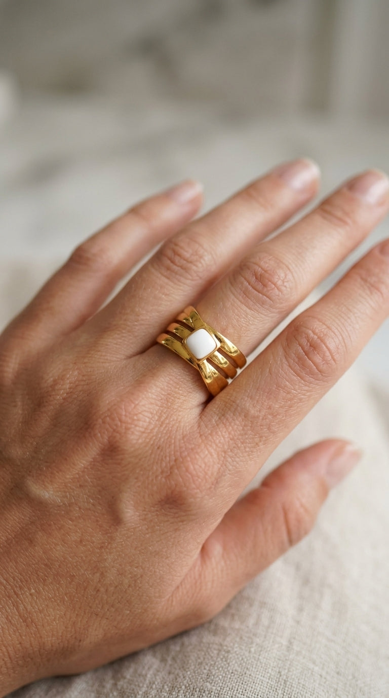 Gold ring with a white stone on a hand against a neutral background