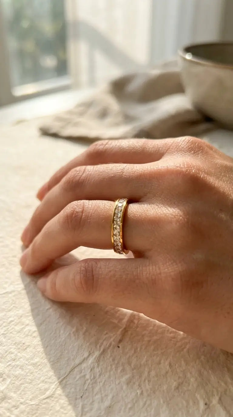 Hand wearing a gold ring on a light surface with a blurred background