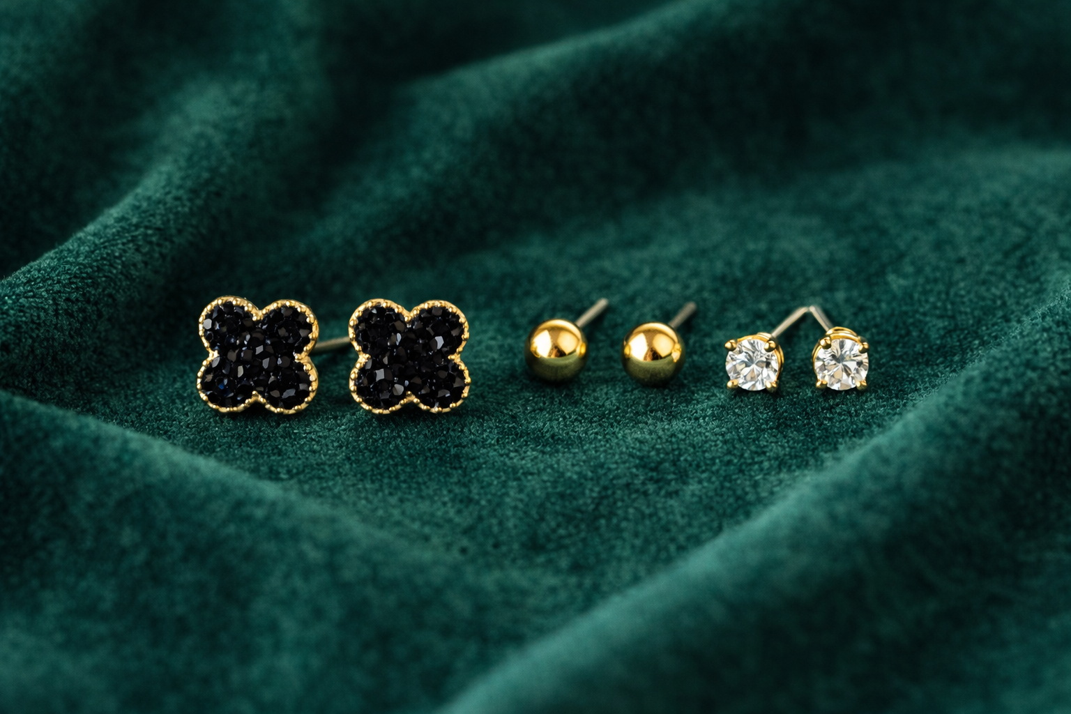 Pair of black flower-shaped earrings and two gold stud earrings on a green fabric background