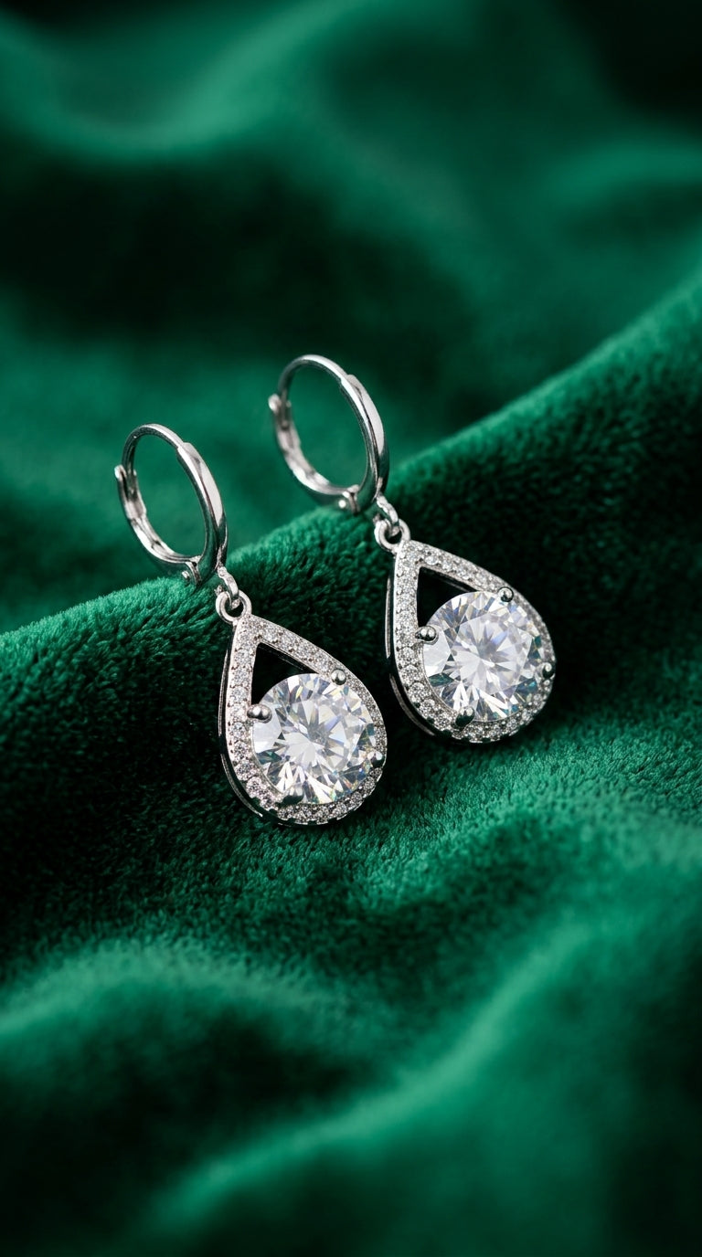 Pair of silver teardrop earrings on a green fabric background